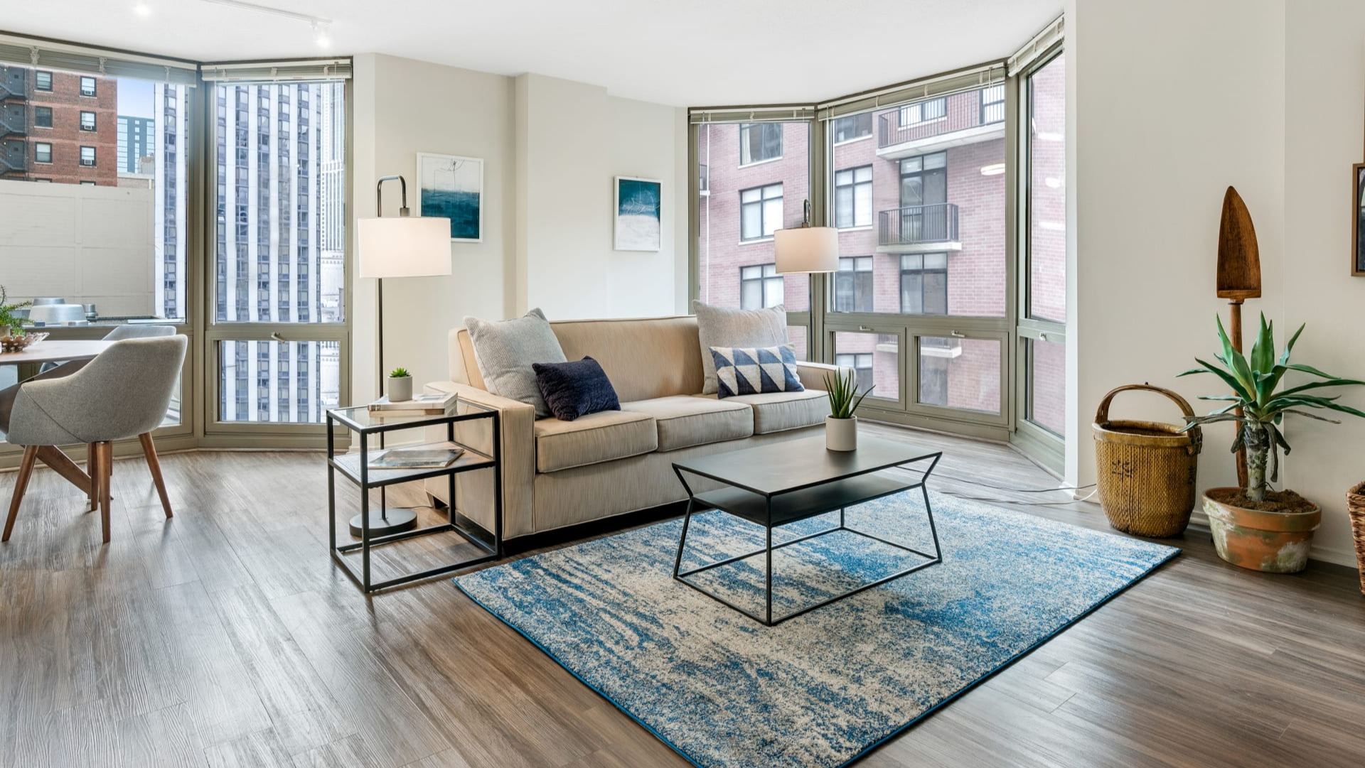 Bright living space with large bay windows, a comfortable sofa, and a vibrant blue rug at Elm Street Plaza Chicago