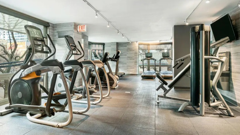 Well-equipped fitness center featuring various cardio machines and large windows at Elm Street Plaza Chicago