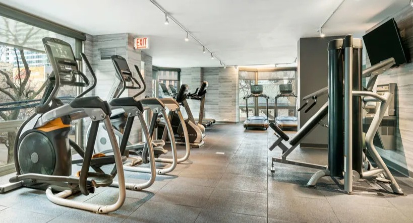 Well-equipped fitness center featuring various cardio machines and large windows at Elm Street Plaza Chicago