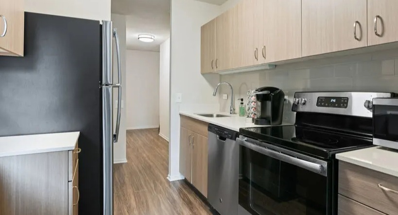 Functional galley kitchen with stainless steel appliances, light wood cabinets, and ample counter space at Elm Street Plaza Chicago