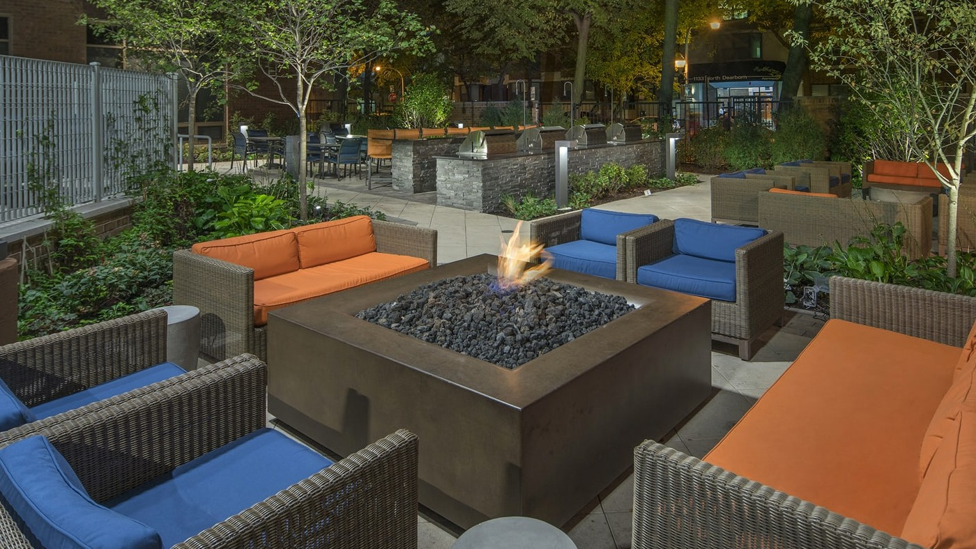 Inviting outdoor fire pit lounge area with comfortable seating and lush landscaping at Elm Street Plaza Chicago