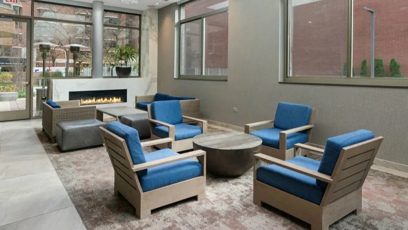 Inviting resident lounge with a fireplace, comfortable blue chairs, and natural light from large windows at Elm Street Plaza Chicago