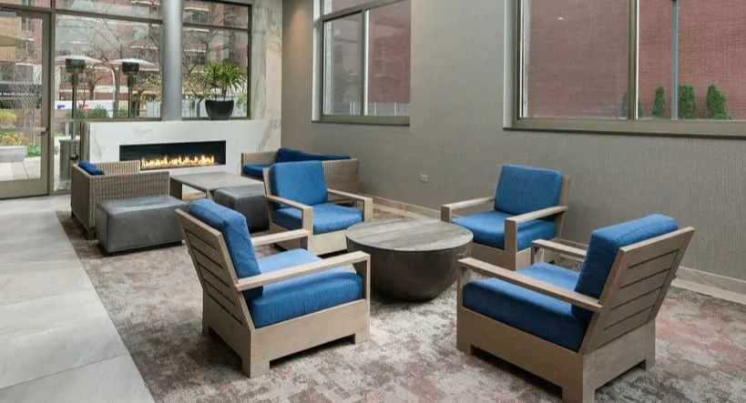 Inviting resident lounge with a fireplace, comfortable blue chairs, and natural light from large windows at Elm Street Plaza Chicago
