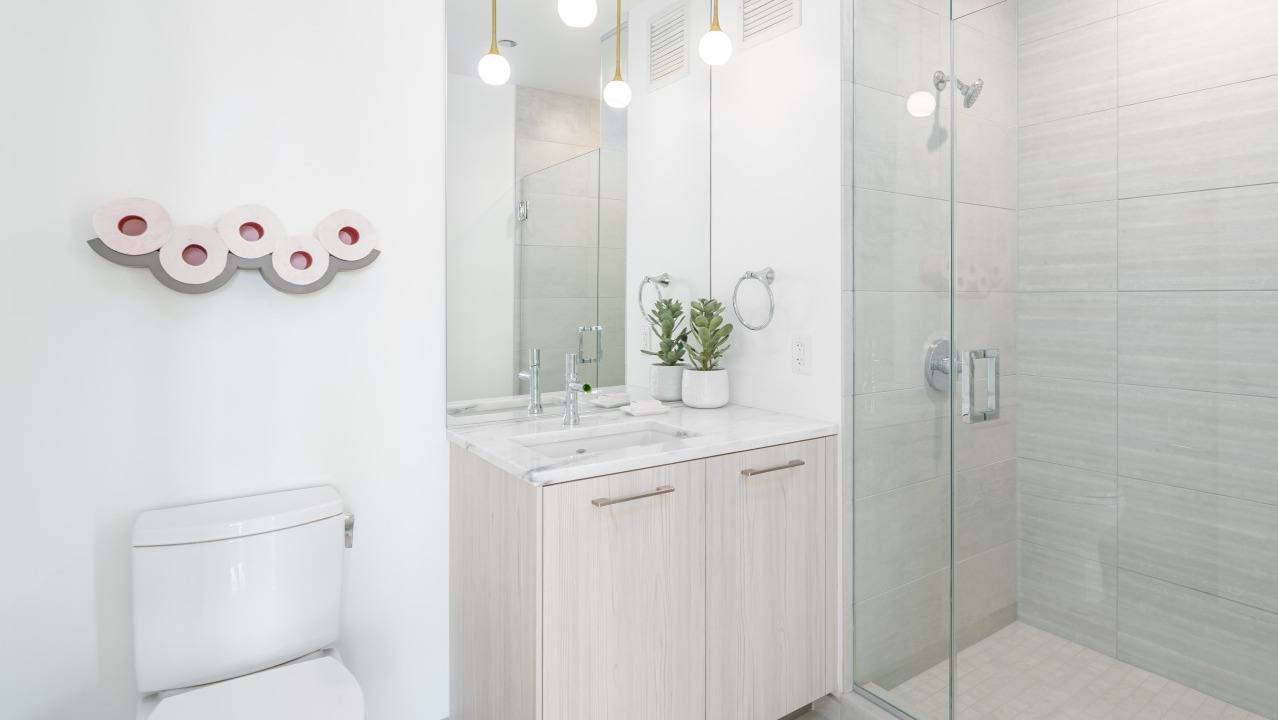 Bright modern bathroom with a glass-enclosed shower, white vanity, stylish mirror, and contemporary lighting at EMME Chicago in Chicago
