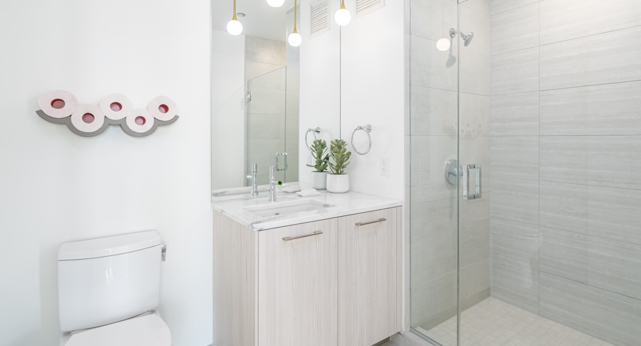 Bright modern bathroom with a glass-enclosed shower, white vanity, stylish mirror, and contemporary lighting at EMME Chicago in Chicago