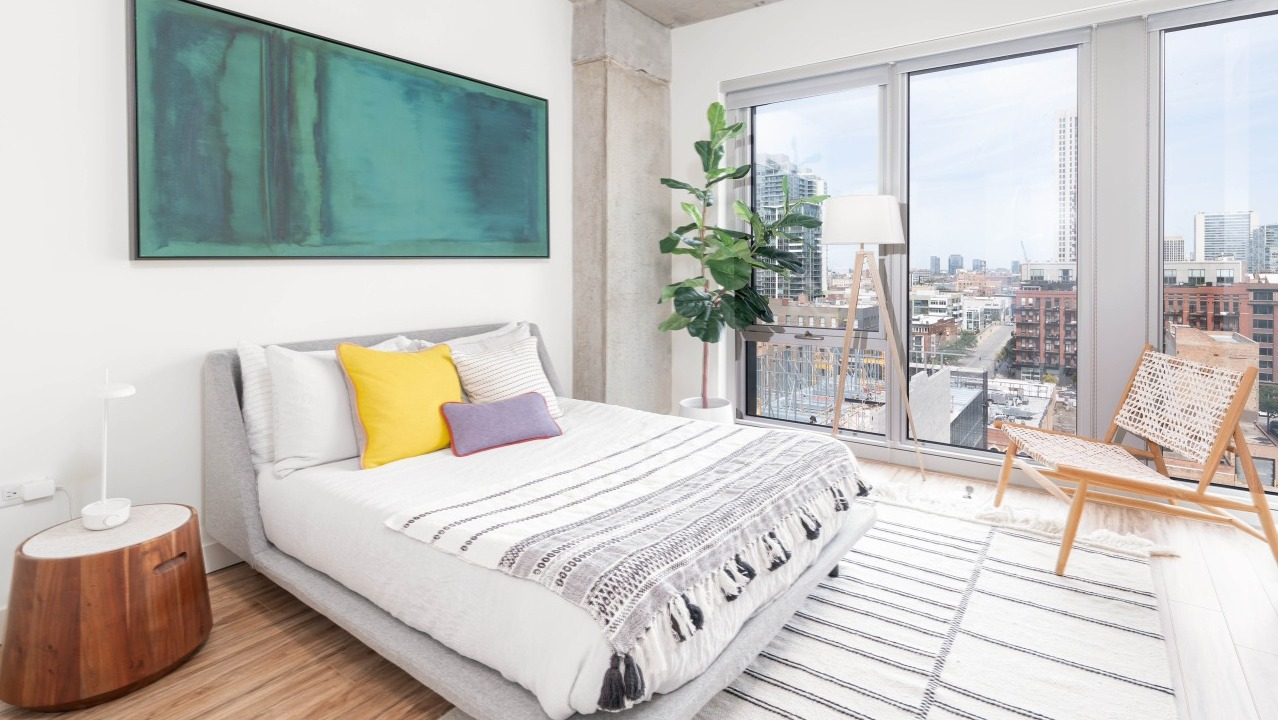Modern bedroom with a comfortable bed, vibrant decor, and large windows offering panoramic cityscape views at EMME Chicago in Chicago