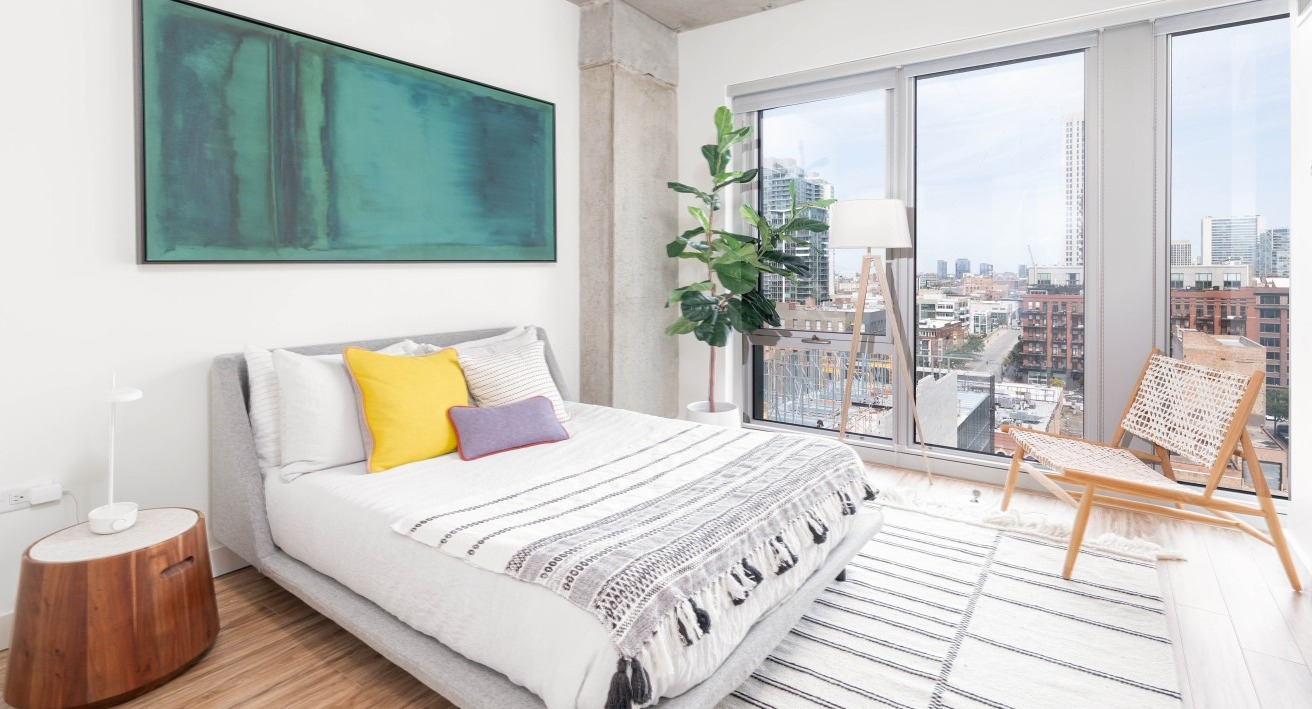 Modern bedroom with a comfortable bed, vibrant decor, and large windows offering panoramic cityscape views at EMME Chicago in Chicago