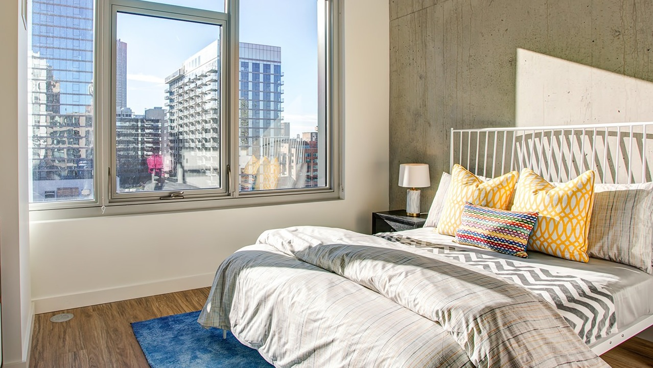 Inviting bedroom with a comfortable bed, industrial-chic concrete accents, and large windows with urban city views at EMME Chicago in Chicago