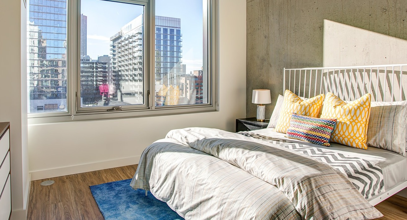 Inviting bedroom with a comfortable bed, industrial-chic concrete accents, and large windows with urban city views at EMME Chicago in Chicago