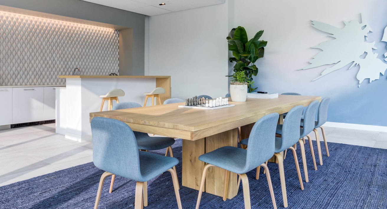 Bright community kitchen and lounge area with a long wooden table, seating, and modern kitchen facilities at EMME Chicago in Chicago