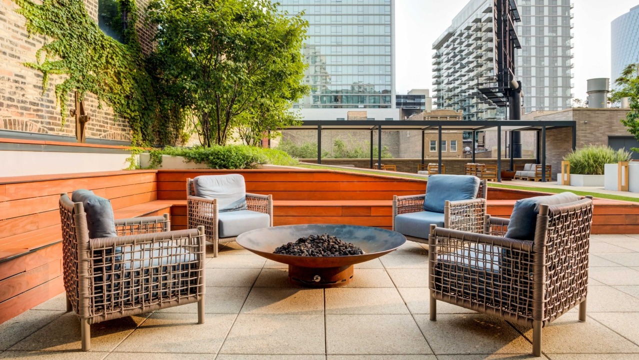 Inviting outdoor courtyard with a central fire pit, comfortable lounge seating, and lush greenery at EMME Chicago in Chicago