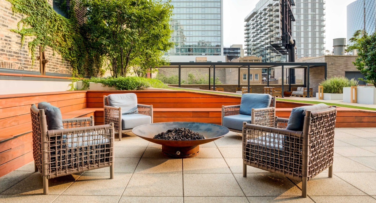 Inviting outdoor courtyard with a central fire pit, comfortable lounge seating, and lush greenery at EMME Chicago in Chicago