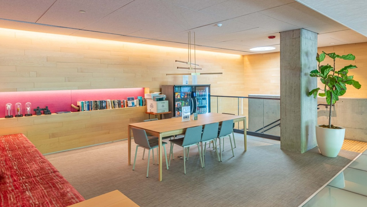 Modern coworking space with a large communal table, comfortable seating, and amenities like a mini-fridge at EMME Chicago in Chicago