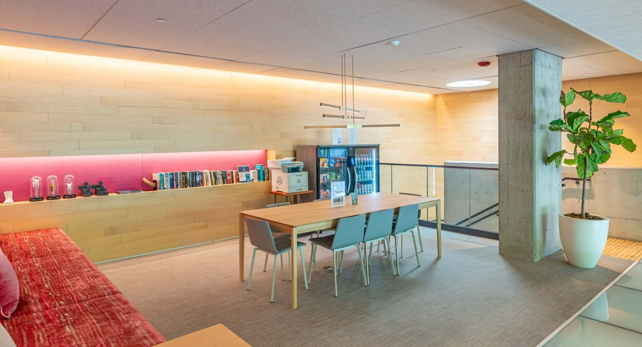 Modern coworking space with a large communal table, comfortable seating, and amenities like a mini-fridge at EMME Chicago in Chicago