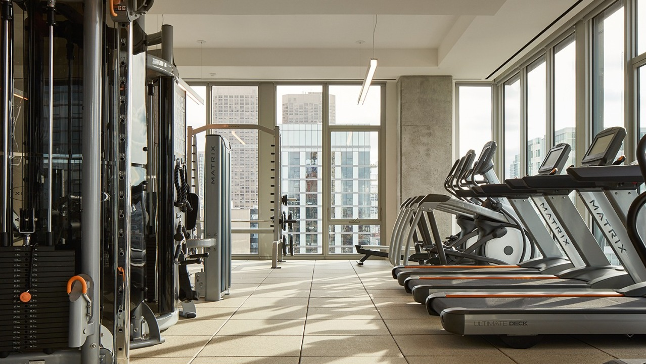 State-of-the-art fitness center with a row of treadmills and various cardio equipment, overlooking city views at EMME Chicago in Chicago