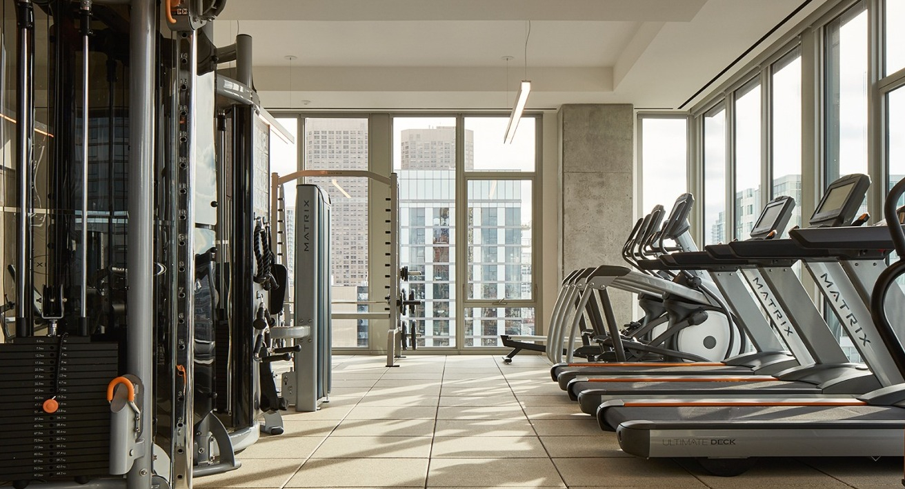 State-of-the-art fitness center with a row of treadmills and various cardio equipment, overlooking city views at EMME Chicago in Chicago