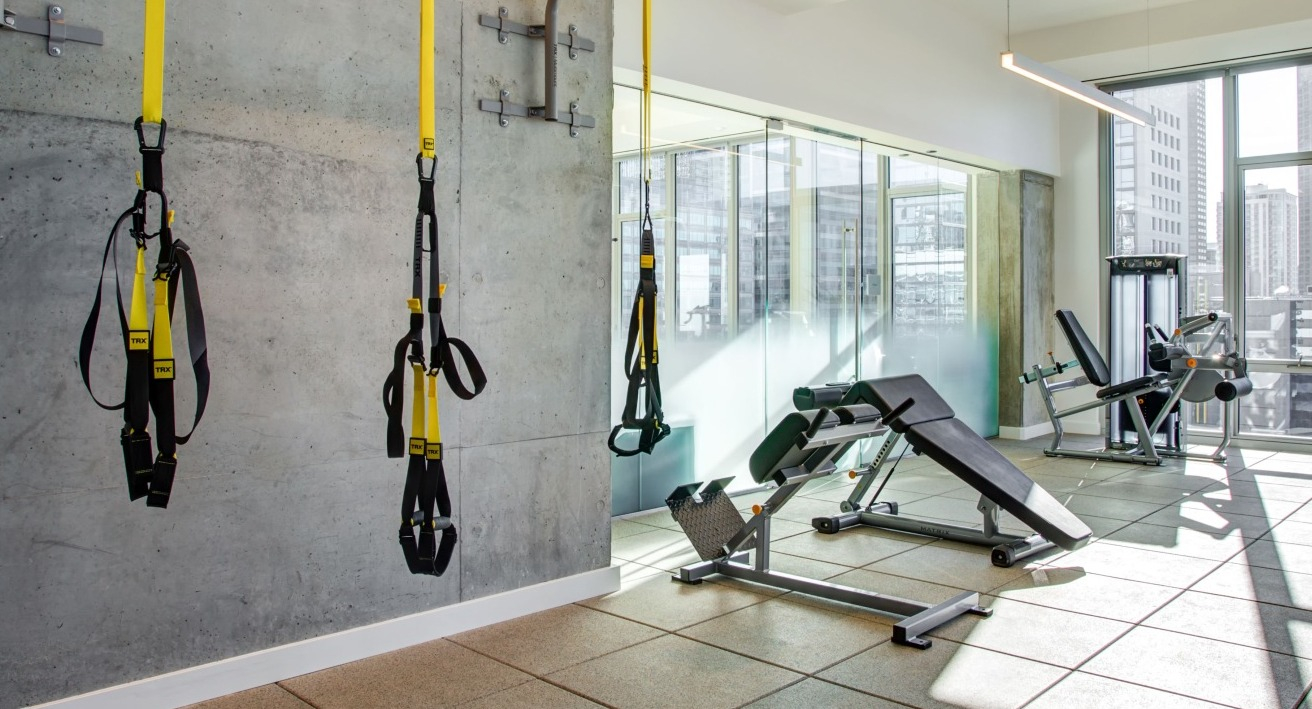 Modern gym area featuring TRX suspension trainers, a weight bench, and strength training equipment with city views at EMME Chicago in Chicago