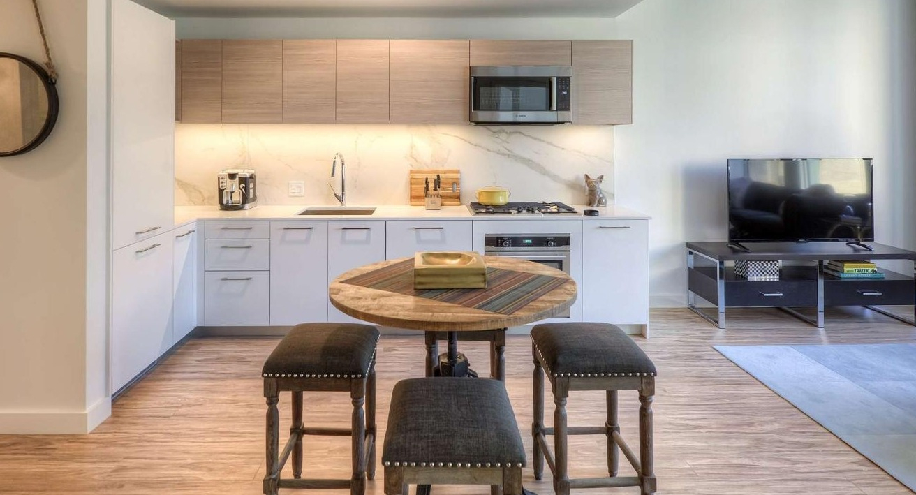Compact and stylish kitchen with modern appliances, a circular dining table, and bar stools, integrated with the living area at EMME Chicago in Chicago