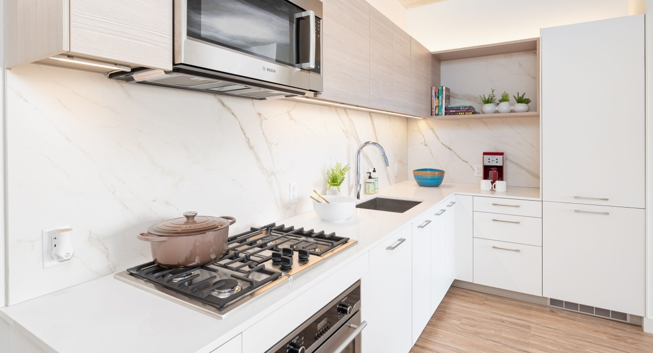 Gourmet kitchen featuring high-end stainless steel appliances, marble backsplash, ample cabinetry, and a gas range at EMME Chicago in Chicago
