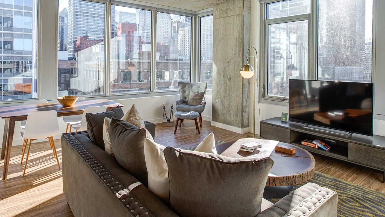 Open-concept living and dining area with comfortable seating, a dining table, and large windows showcasing city views at EMME Chicago in Chicago