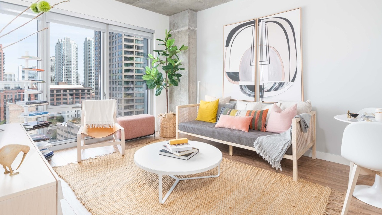 Bright and airy living room with a comfortable sofa, natural fiber rug, modern art, and expansive city views at EMME Chicago in Chicago