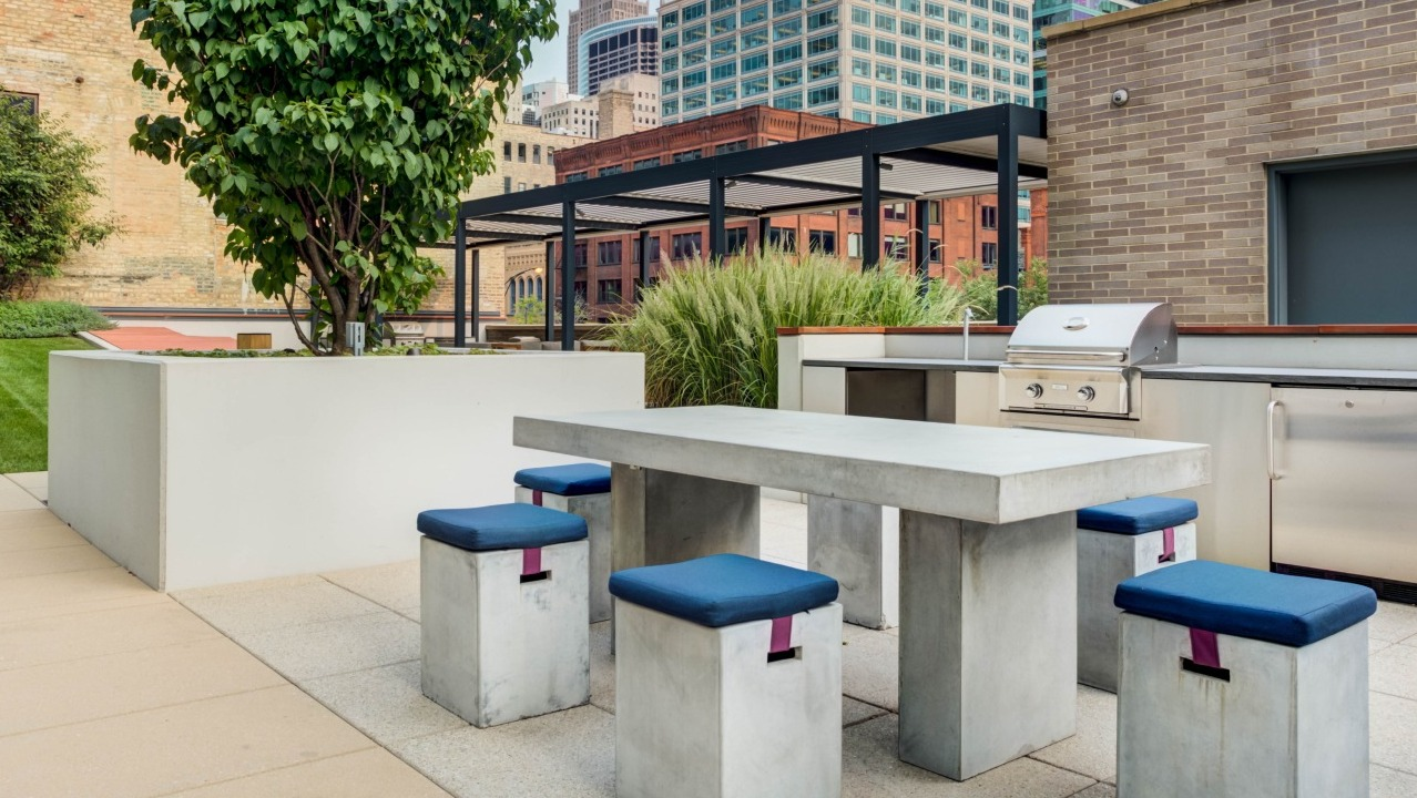 Modern outdoor dining area with a concrete table, stools, and a high-end grill station amidst greenery at EMME Chicago in Chicago