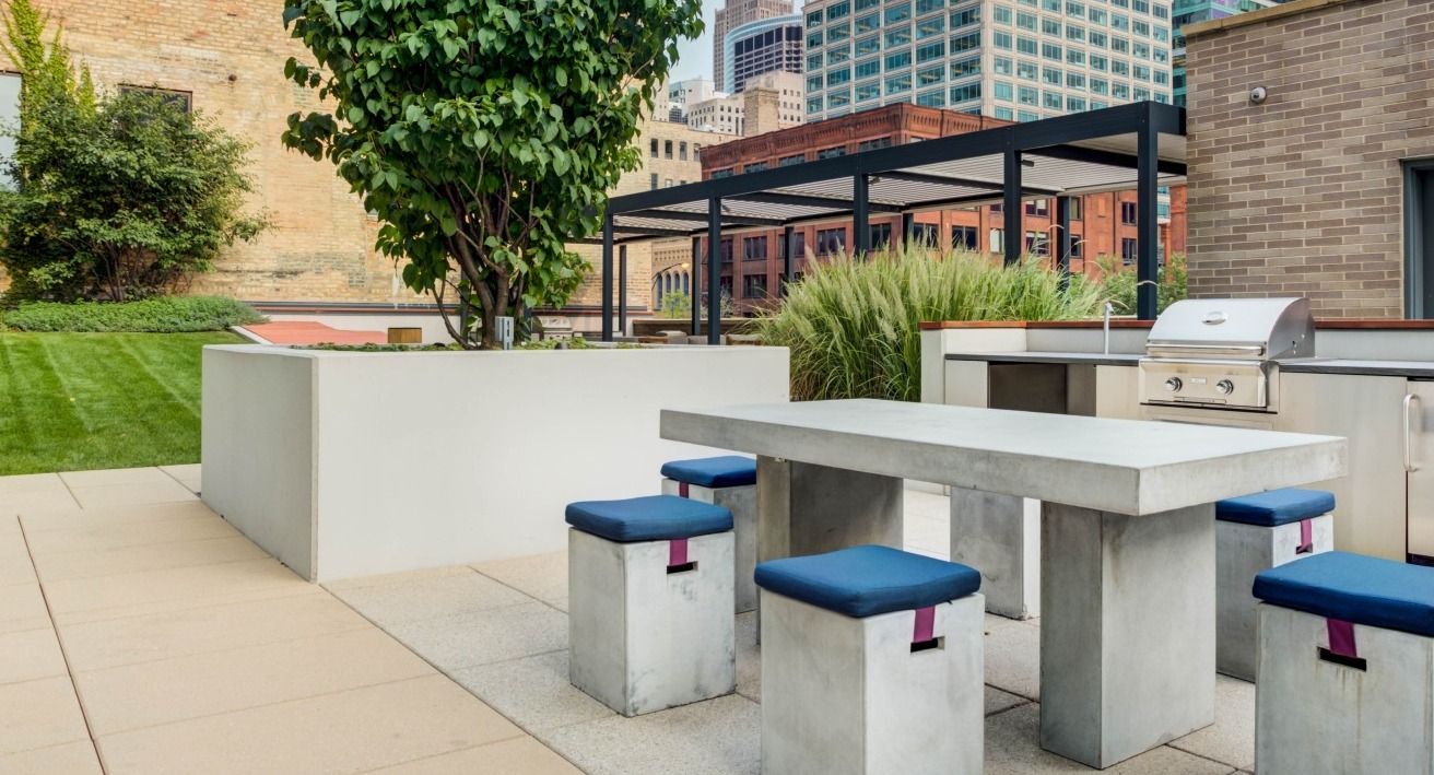 Modern outdoor dining area with a concrete table, stools, and a high-end grill station amidst greenery at EMME Chicago in Chicago