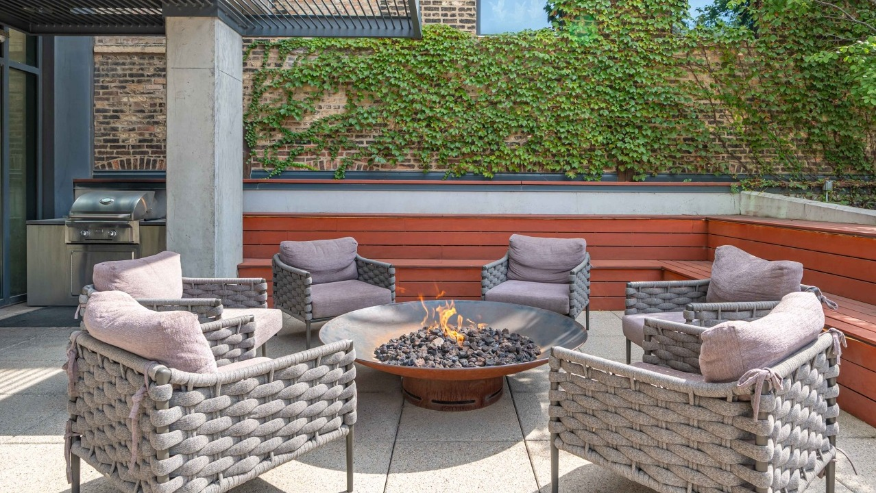 Inviting outdoor lounge area with a cozy fire pit, comfortable seating, and a built-in grill station at EMME Chicago in Chicago