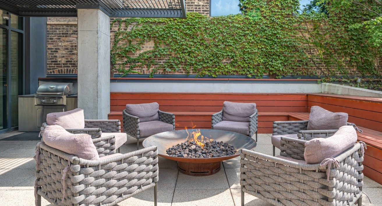 Inviting outdoor lounge area with a cozy fire pit, comfortable seating, and a built-in grill station at EMME Chicago in Chicago