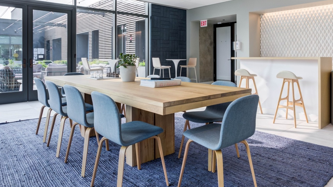 Spacious resident lounge with a long communal dining table, comfortable chairs, and a modern bar area at EMME Chicago in Chicago