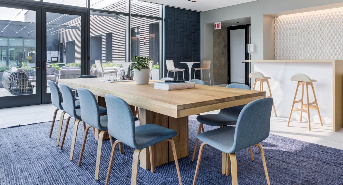 Spacious resident lounge with a long communal dining table, comfortable chairs, and a modern bar area at EMME Chicago in Chicago