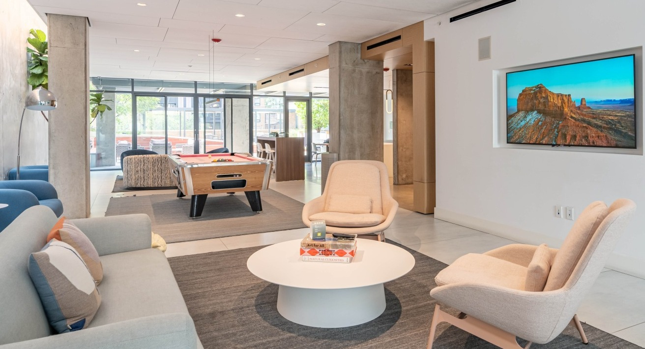 Modern resident lounge featuring a comfortable seating area, a foosball table, and a wall-mounted TV at EMME Chicago in Chicago