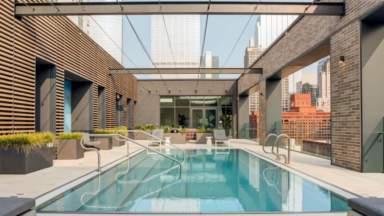 Stunning rooftop swimming pool surrounded by lounge chairs, offering impressive city skyline views at EMME Chicago in Chicago