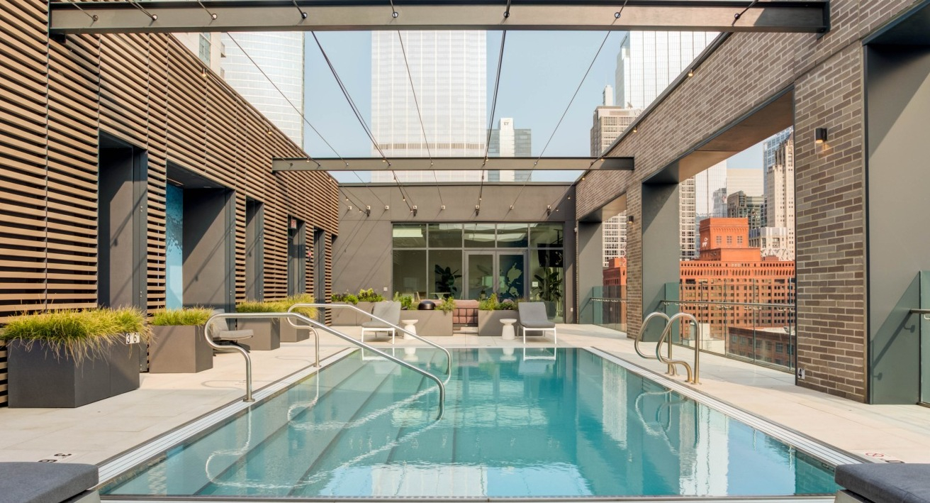 Stunning rooftop swimming pool surrounded by lounge chairs, offering impressive city skyline views at EMME Chicago in Chicago