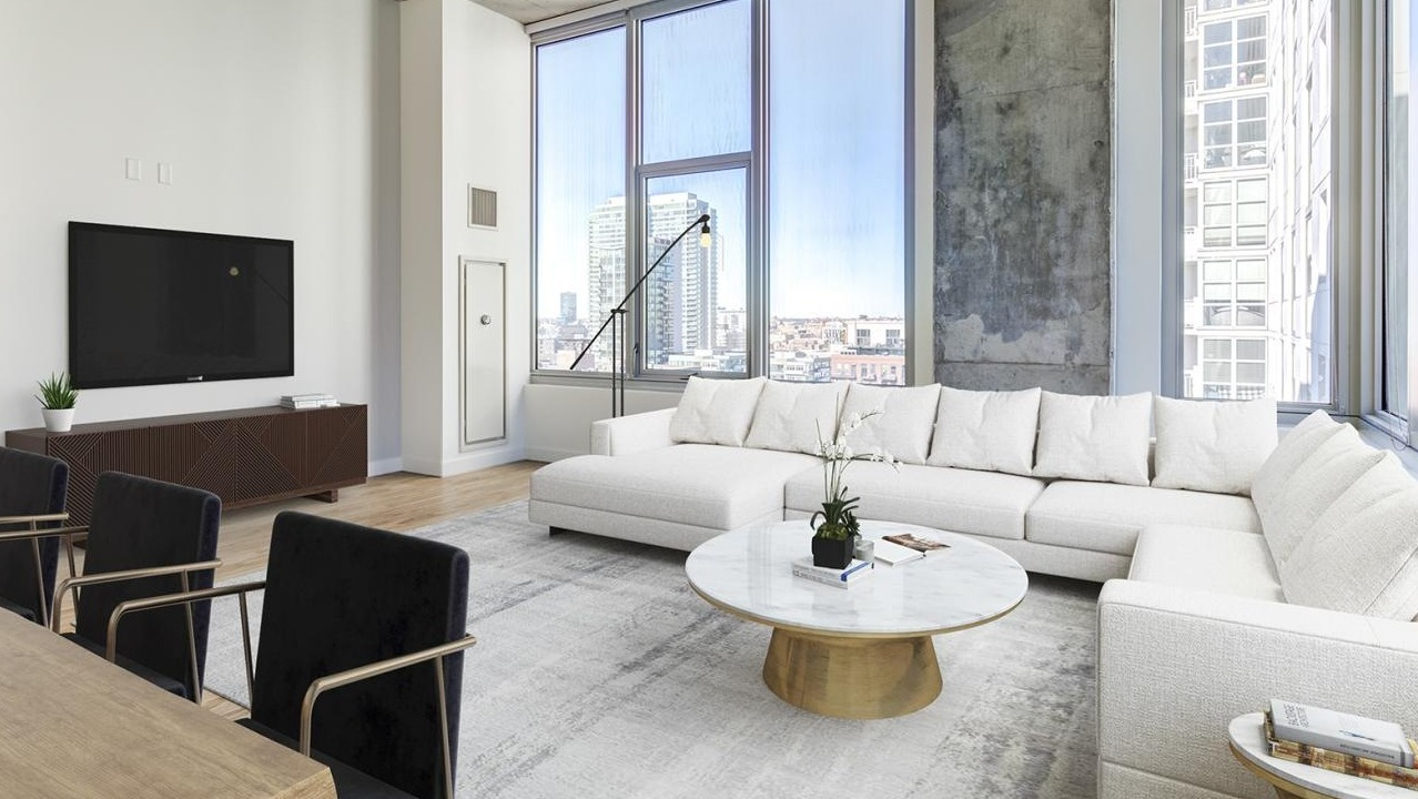 Expansive living room with a large white sectional sofa, modern coffee table, and floor-to-ceiling windows offering city views at EMME Chicago in Chicago
