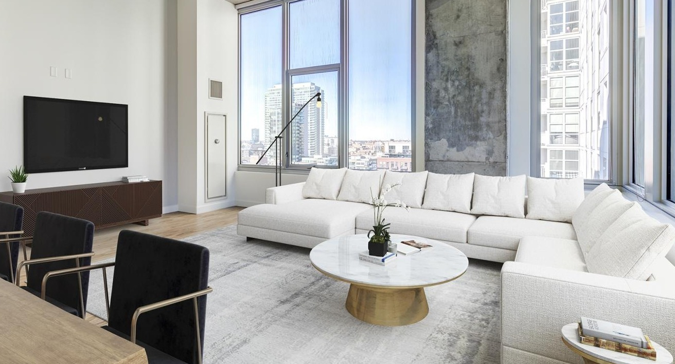 Expansive living room with a large white sectional sofa, modern coffee table, and floor-to-ceiling windows offering city views at EMME Chicago in Chicago