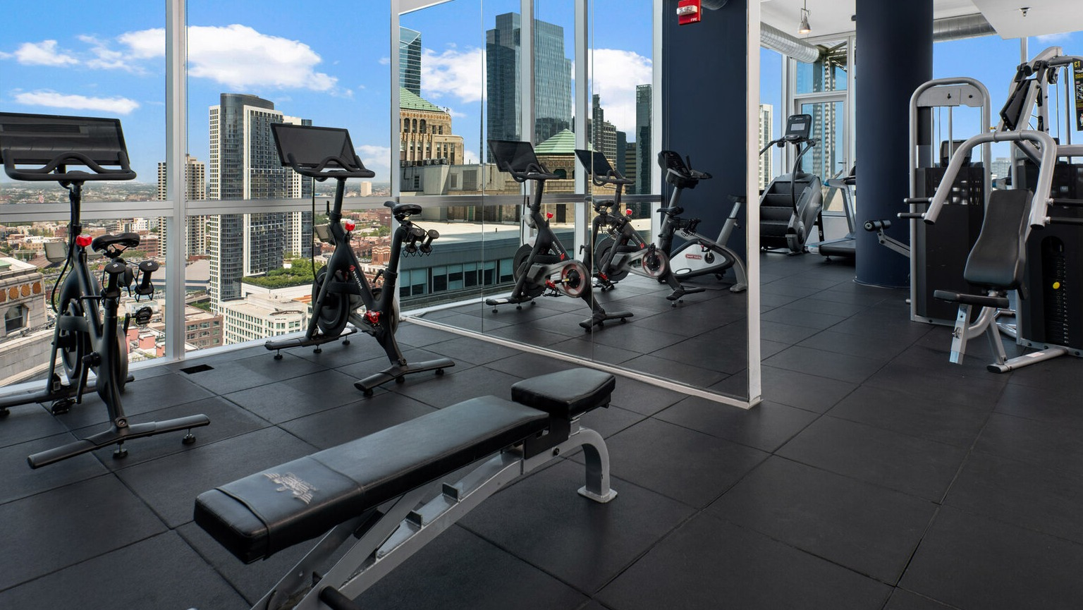 Spacious gym at Env Chicago with various cardio and weight machines, plus expansive city skyline views
