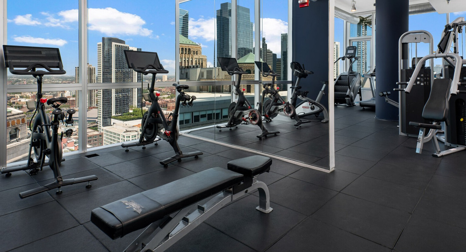 Spacious gym at Env Chicago with various cardio and weight machines, plus expansive city skyline views