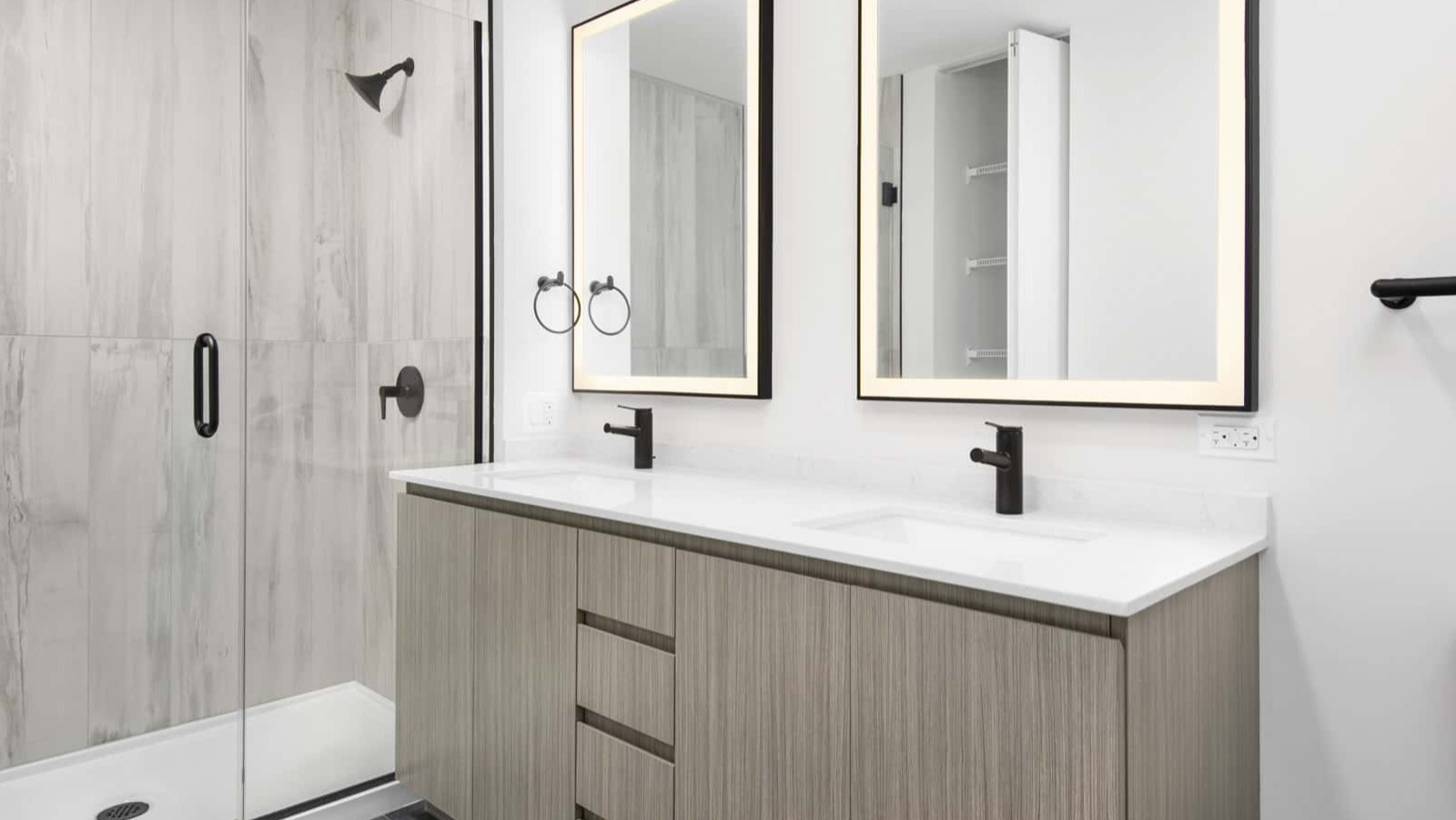 Sleek apartment bathroom at Evo Union Park in Chicago, with a light wood double vanity, illuminated mirrors, and a spacious walk-in shower