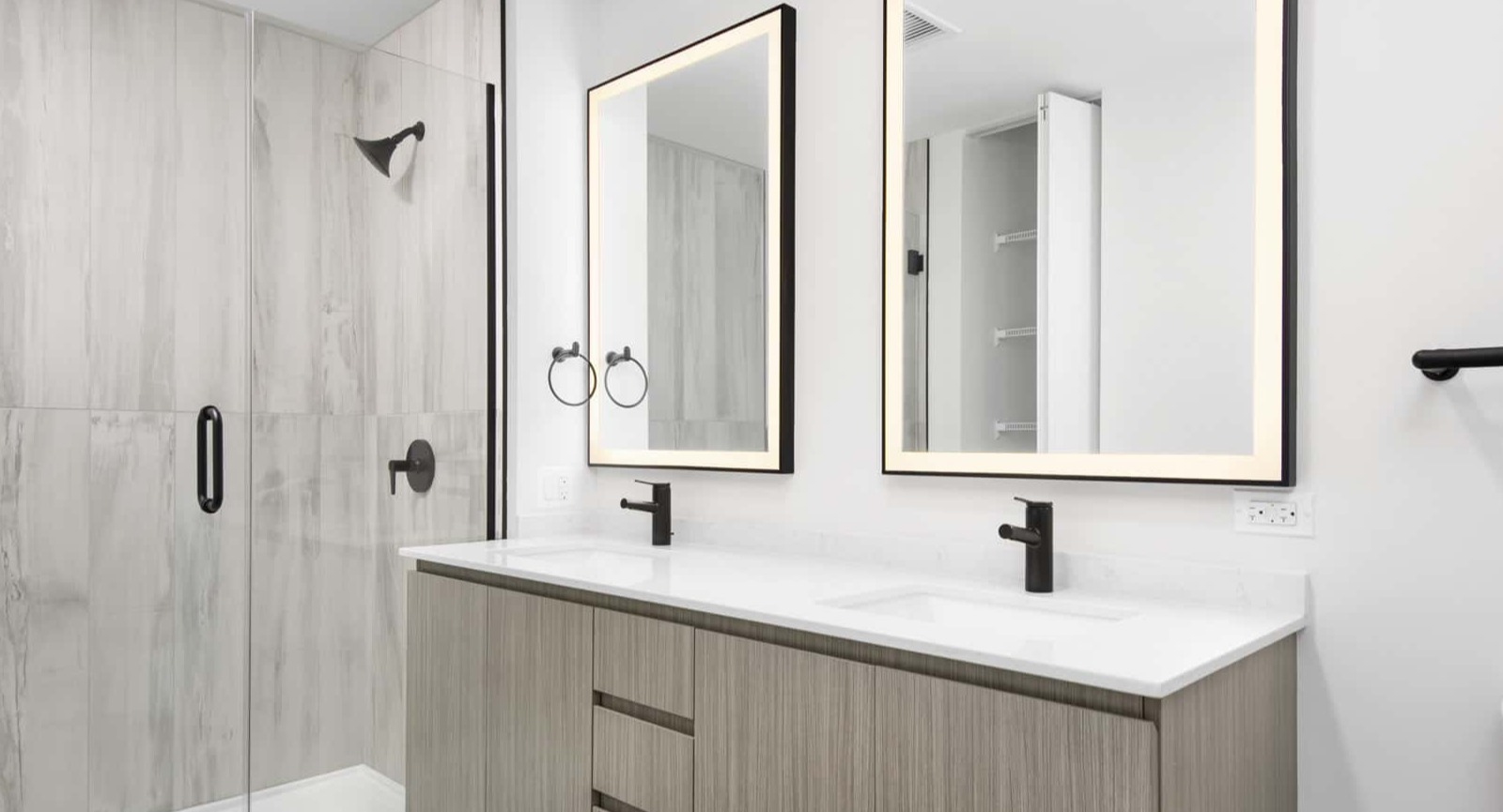 Sleek apartment bathroom at Evo Union Park in Chicago, with a light wood double vanity, illuminated mirrors, and a spacious walk-in shower