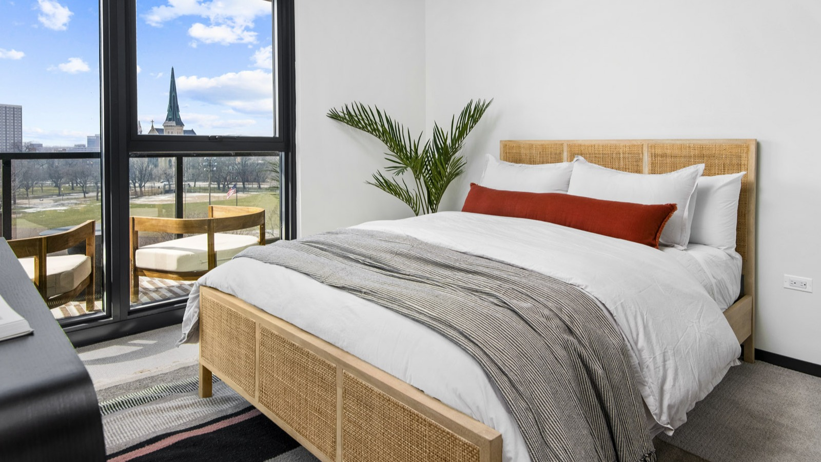 Cozy apartment bedroom at Evo Union Park in Chicago, featuring a natural wood bed frame, large windows, and a private balcony overlooking the city