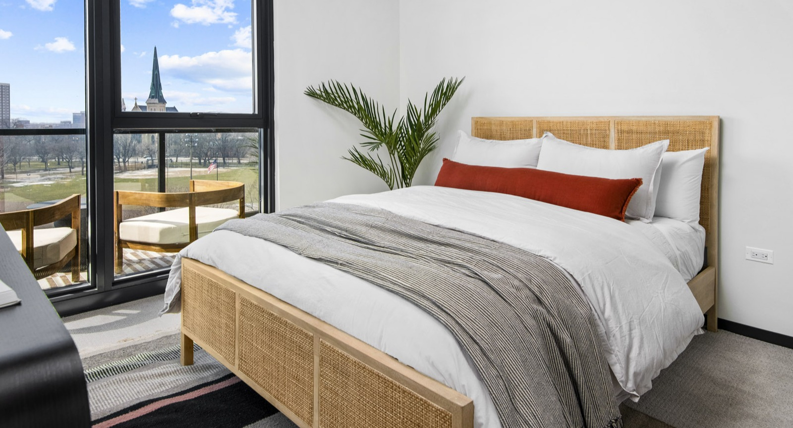 Cozy apartment bedroom at Evo Union Park in Chicago, featuring a natural wood bed frame, large windows, and a private balcony overlooking the city