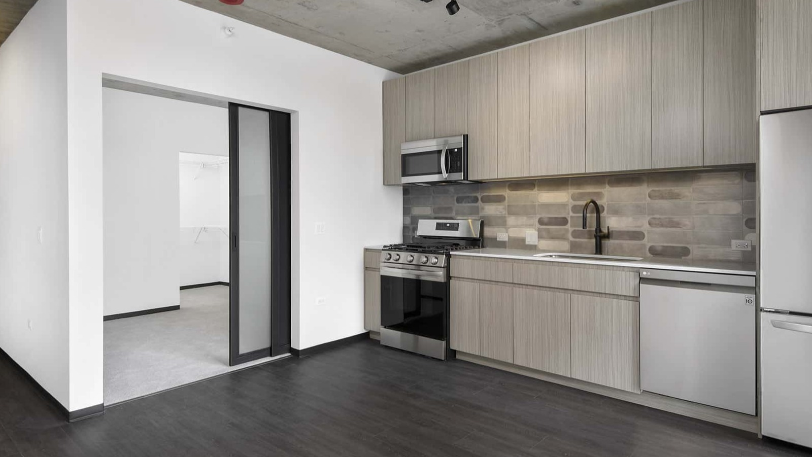 Modern apartment kitchen at Evo Union Park in Chicago, featuring light wood cabinetry, stainless steel appliances, and an entryway leading to another room