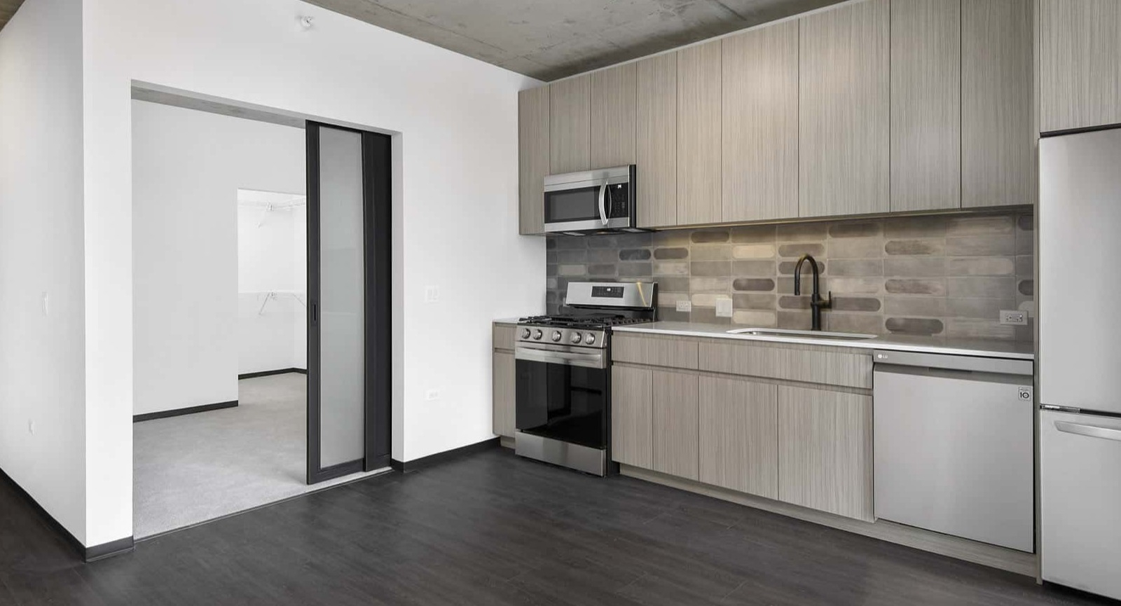 Modern apartment kitchen at Evo Union Park in Chicago, featuring light wood cabinetry, stainless steel appliances, and an entryway leading to another room