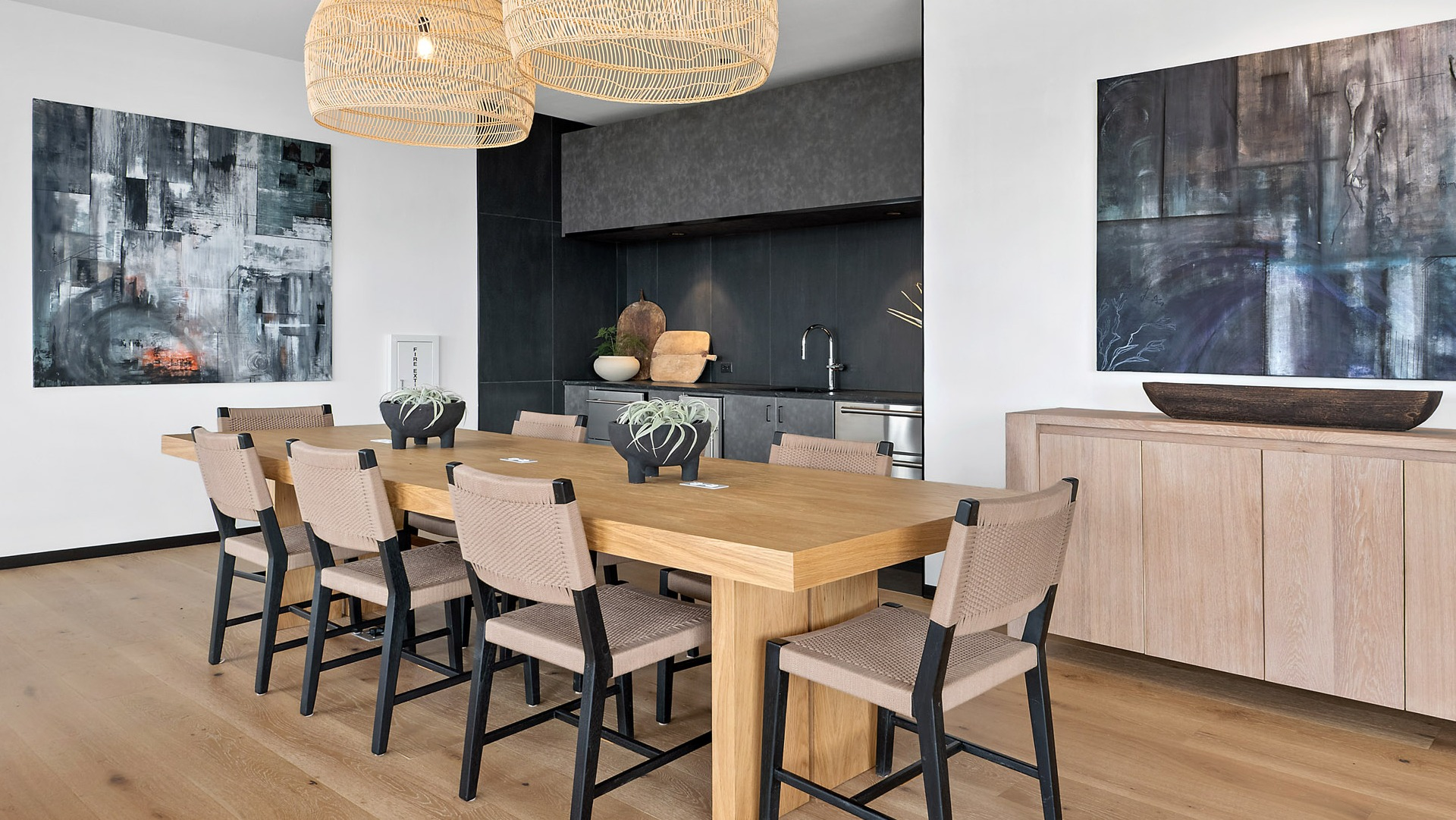 Elegant private dining room and chef's kitchen at Evo Union Park in Chicago, with a large wood table, woven light fixtures, and modern art