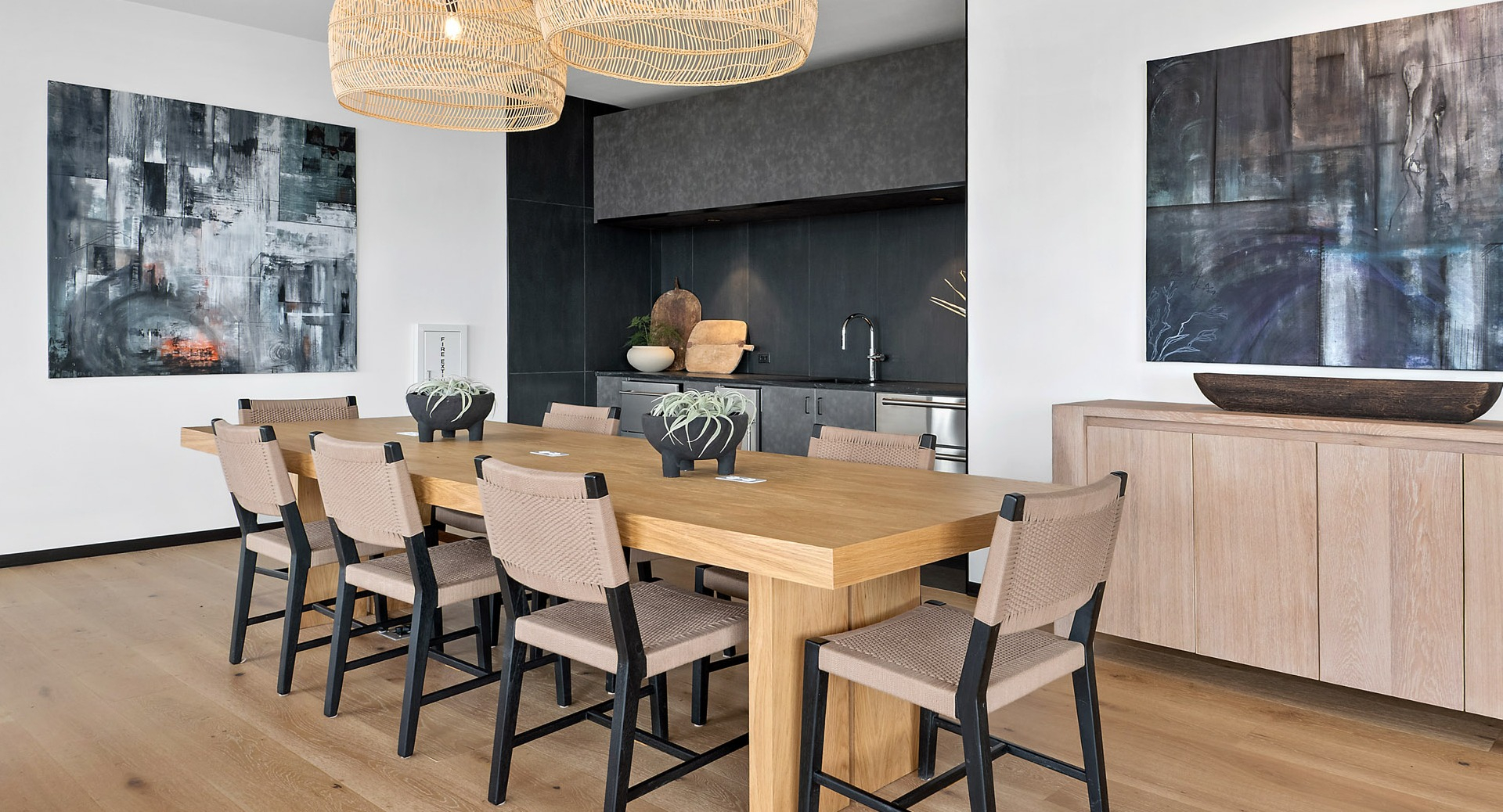 Elegant private dining room and chef's kitchen at Evo Union Park in Chicago, with a large wood table, woven light fixtures, and modern art