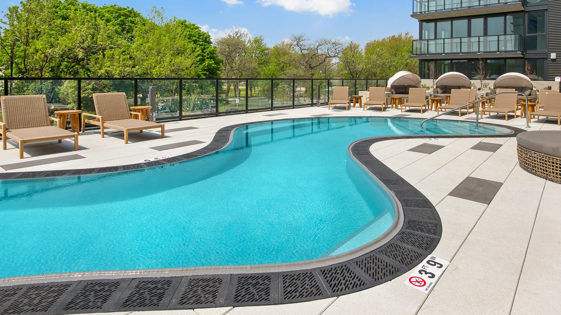 Panoramic view of the outdoor pool area at Evo Union Park in Chicago, showcasing the modern building exterior and lush green surroundings