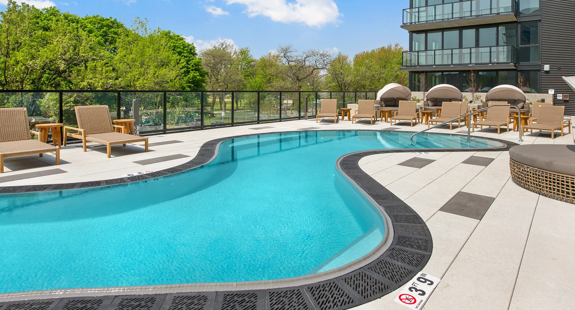 Panoramic view of the outdoor pool area at Evo Union Park in Chicago, showcasing the modern building exterior and lush green surroundings