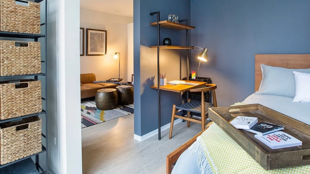 Cozy bedroom featuring a comfortable bed and a functional desk area, with a view into the living space at Exhibit on Superior in Chicago