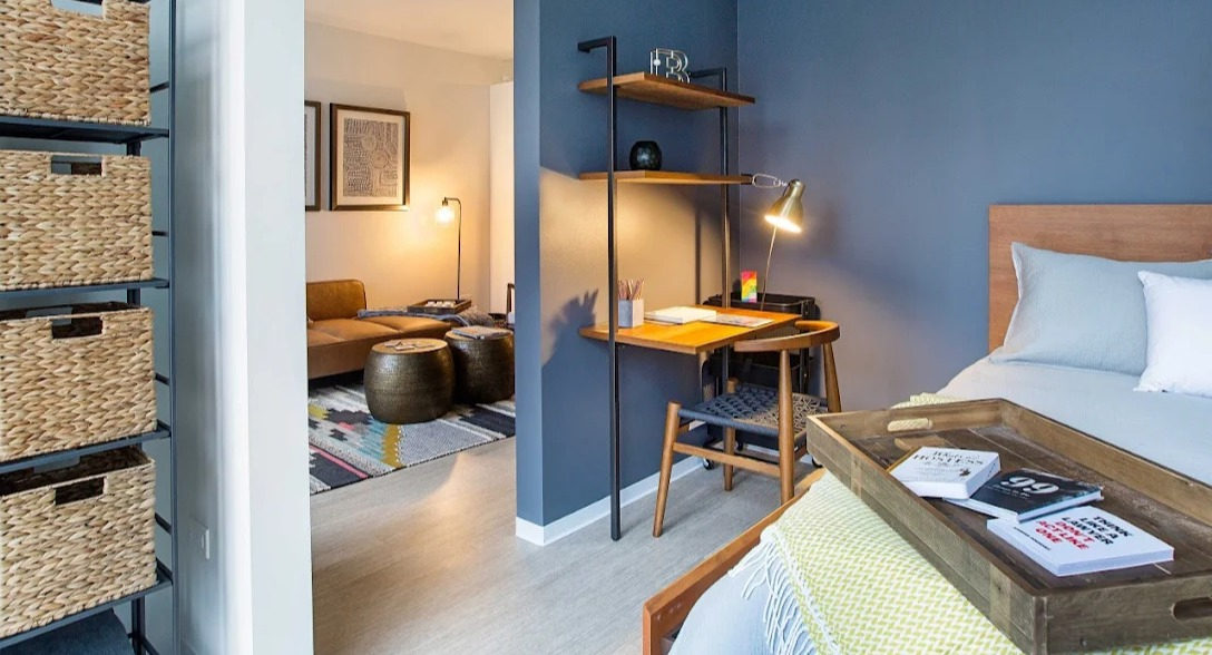 Cozy bedroom featuring a comfortable bed and a functional desk area, with a view into the living space at Exhibit on Superior in Chicago